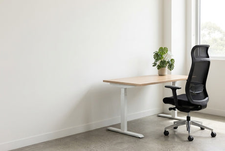 Black mesh ergonomic chair beside an oak sit-stand desk