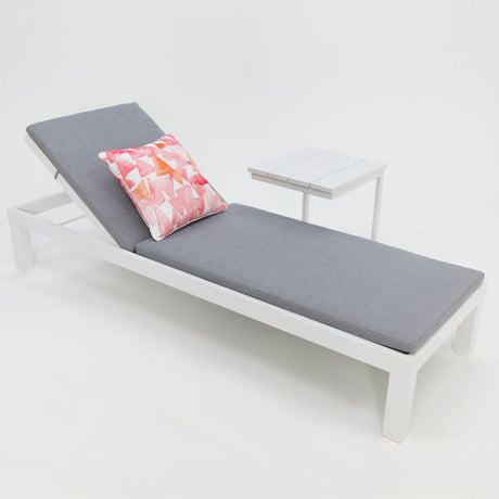 White sun lounge and table setting positioned beside a swimming pool