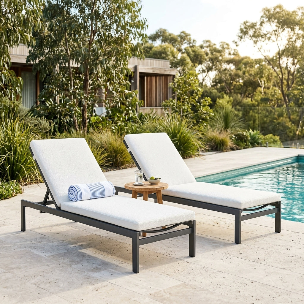 Two aluminium sun lounges with side table beside a pool